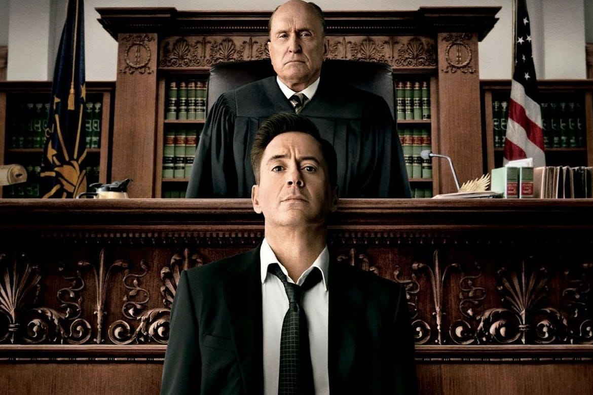 Na imagem: Robert Downey Jr. olha para câmera em frente ao estrado de seu pai, que está num plano acima, caracterizado como juiz. 