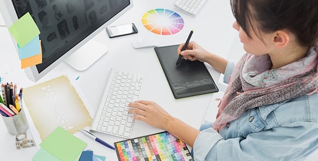 Na imagem: designer trabalha com tablet e computador em um projeto cercado de cartela de cores