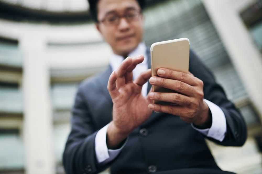 Na imagem: homem de terno usa celular para praticar alguma ação