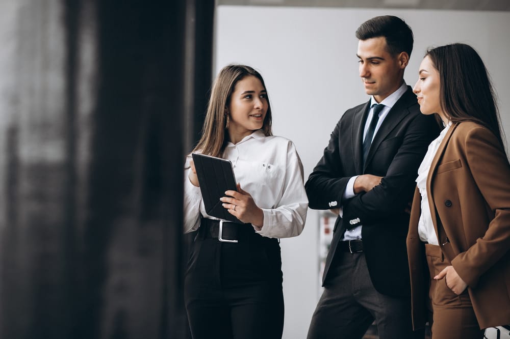 Na imagem: três pessoas em ambiente profissional conversam entre si com seriedade