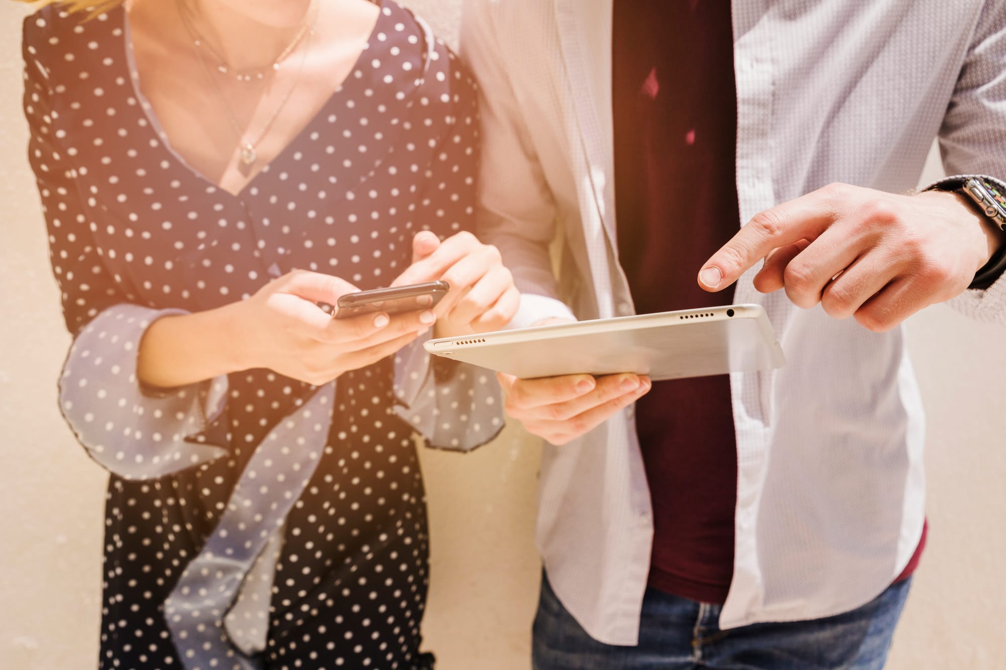 Na imagem: duas pessoas checam respectivamente seu smartphone e seu tablet