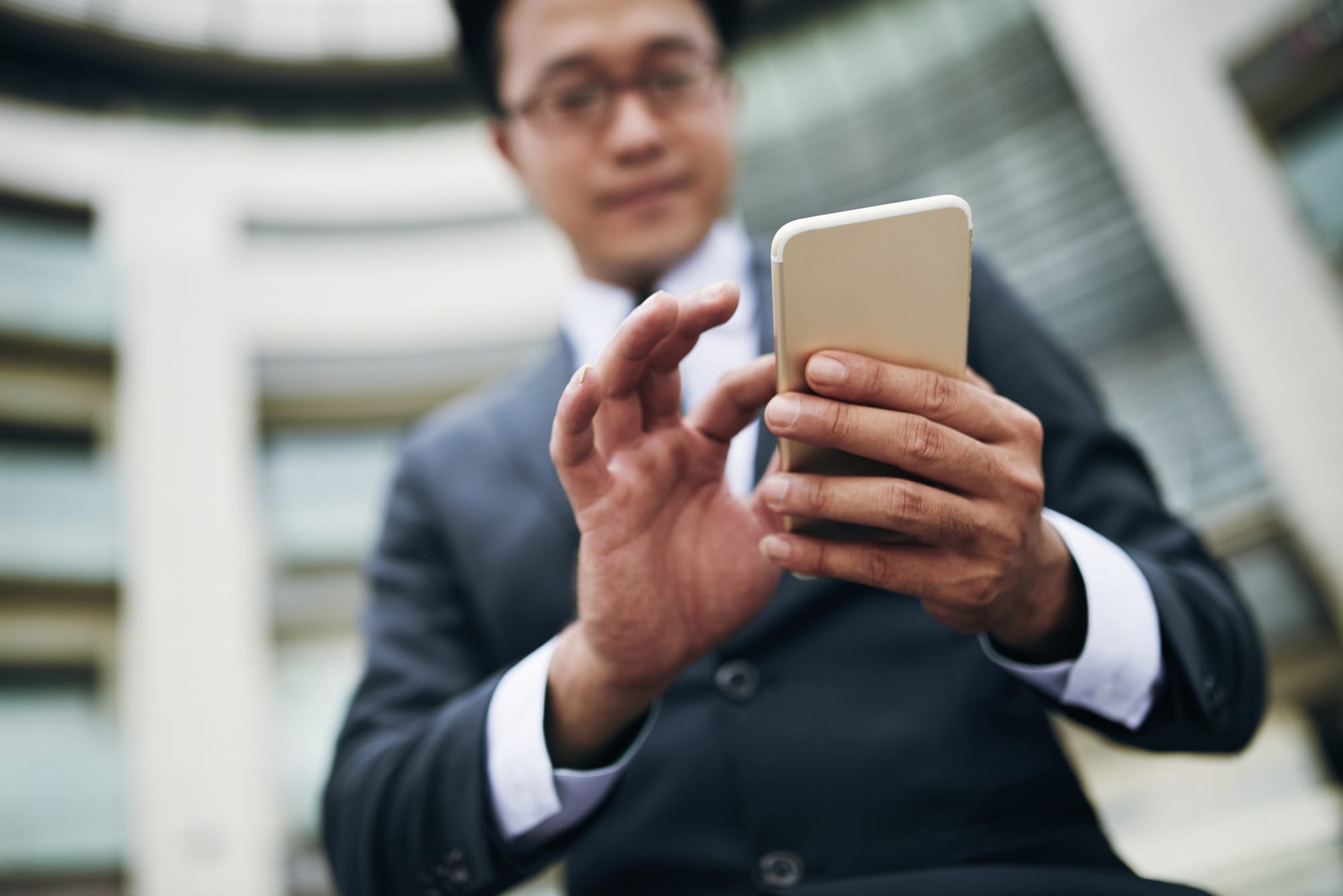 Na foto: Homem de terno usa celular para praticar alguma ação.