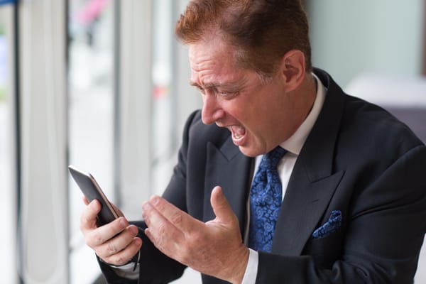 Na imagem: homem de terno aparenta estar revoltado com o que leu em seu smartphone