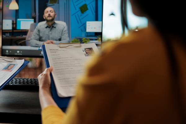 Na imagem: recrutadora olha para candidato com seu currículo em mãos.