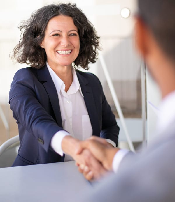 Na imagem: advogado aperta mão de uma cliente mulher que abre um grande sorriso ao olhar em seus olhos.